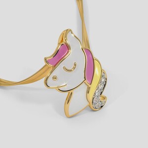 May include: A gold-toned necklace featuring a unicorn pendant. The pendant has a white face, pink mane, and yellow accents, with a section of clear crystals. The necklace chain is a woven design.