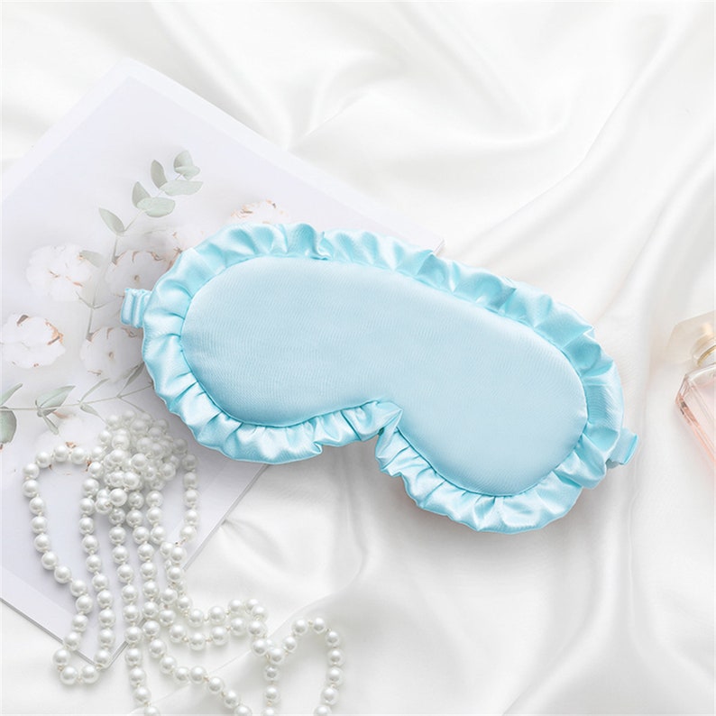 May include: A light blue sleep mask with a ruffled edge. The mask is made of a soft, silky material.