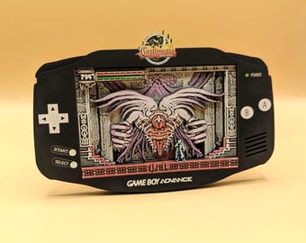 May include: A black Game Boy Advance shadow box display featuring a 3D layered scene from Castlevania: Aria of Sorrow. The screen area shows a boss battle with a large winged creature and a small character, with the Castlevania logo at the top.