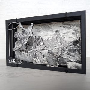 May include: A black framed 3D art piece featuring a detailed grayscale depiction of a figure in action, set against a backdrop of traditional Japanese architecture. The text "SEKIRO SHADOWS DIE TWICE" is visible.
