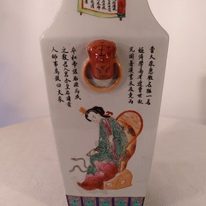 Pode incluir: Um vaso de porcelana branca com base quadrada e boca larga. O vaso é decorado com um desenho floral colorido e caracteres chineses. O vaso tem aproximadamente 30 cm de altura.