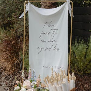 May include: A white ceramic mug with a black handle and the text "But First, Coffee" in a black, handwritten-style font. The mug is on a white surface.
