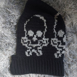 Op de afbeelding: Zwarte gebreide beanie met een wit schedelontwerp. De schedel wordt twee keer op de beanie herhaald.