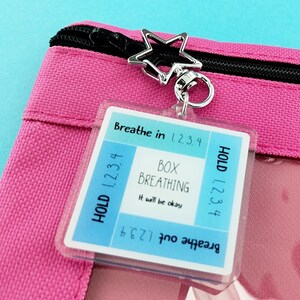 May include: A pink zippered pouch with a star-shaped charm. A clear tag attached reads "Breathe in 1.2.3.4, Hold 1.2.3.4, Box Breathing, It will be okay, Breathe out 1.2.3.4". The pouch is made of a textured fabric.