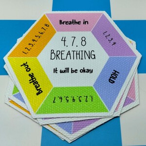 May include: A hexagonal card featuring a 4, 7, 8 breathing guide. The center text reads 4, 7, 8 BREATHING and It will be okay. Surrounding sections include Breathe in, 1.2.3.4, HOLD, 1.2.3.4.5.6.7, Breathe out, and 1.2.3.4.5.6.7.8 in various colors.