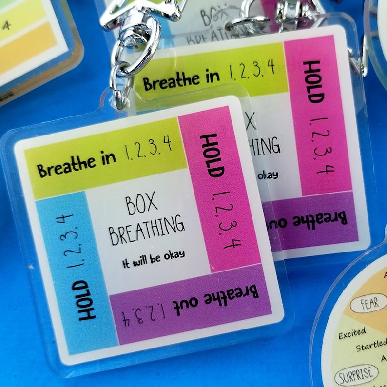 K&ouml;nnte beinhalten: Ein quadratischer Acryl-Schl&uuml;sselanh&auml;nger mit einer Anleitung zur Box-Atmung in farbigen Abschnitten. Der Text lautet: Breathe in 1, 2, 3, 4, HOLD 1, 2, 3, 4, Breathe out 1, 2, 3, 4 und HOLD 1, 2, 3, 4. Der mittlere Text lautet BOX BREATHING und It will be okay.