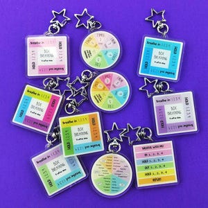 May include: A collection of keychains with various designs and text related to breathing exercises. Some keychains are square with the text "Breathe in 1234, Box Breathing, Hold 1234, Breathe out 1234". Other keychains are round with a color wheel.