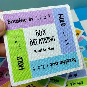 May include: A square card with a textured surface featuring a box breathing guide. The center text reads BOX BREATHING and It will be okay. The border sections include instructions: Breathe in 1, 2, 3, 4; HOLD 1, 2, 3, 4; Breathe out 1, 2, 3, 4; and HOLD 1, 2, 3, 4.