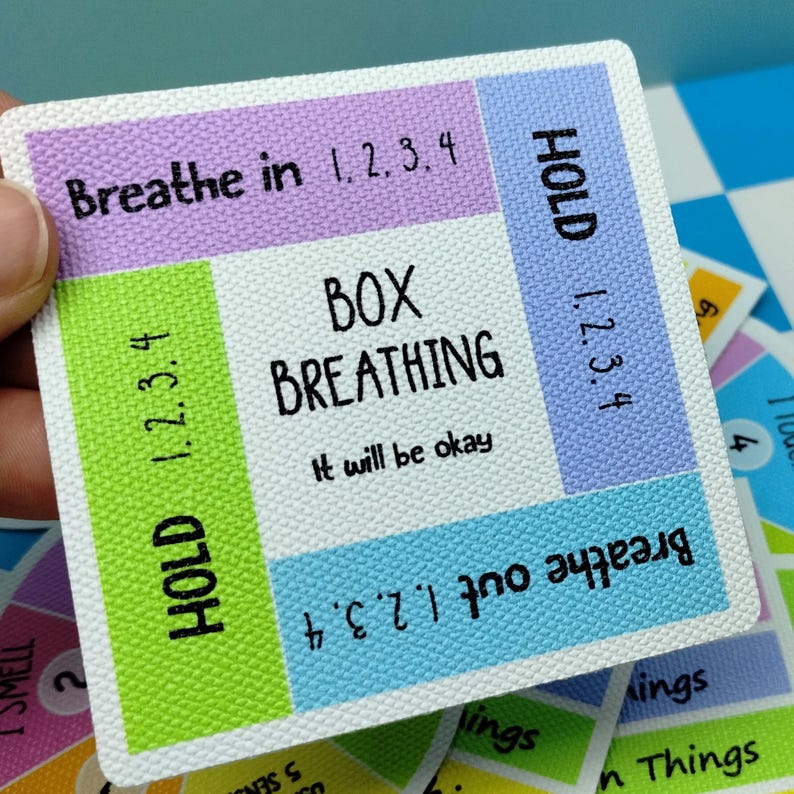 May include: A square card with a textured surface featuring a box breathing guide. The center text reads BOX BREATHING and It will be okay. The border sections include instructions: Breathe in 1, 2, 3, 4; HOLD 1, 2, 3, 4; Breathe out 1, 2, 3, 4; and HOLD 1, 2, 3, 4.