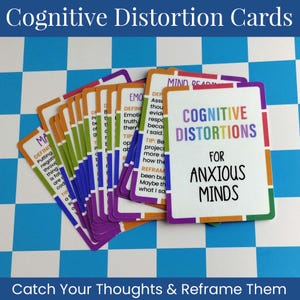 May include: A deck of rectangular Cognitive Distortions for Anxious Minds cards with white backgrounds and colorful borders. Each card features text definitions, tips, and reframing techniques for various cognitive distortions, displayed in a fan arrangement.