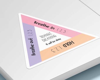 Puede incluir: Una pegatina triangular con borde blanco que presenta secciones en rosa pastel, morado y naranja. El texto dice: Breathe in 1, 2, 3; Breathe out 1, 2, 3; HOLD 1, 2, 3; TRIANGLE BREATHING; It will be okay. La pegatina está sobre una superficie plana.