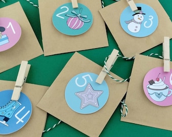 May include: A set of six brown paper envelopes, each clipped with a wooden clothespin to a green and white twine string. Each envelope features a circular tag numbered one through six, decorated with illustrations of a gift, ornament, snowman, skate, star, and cocoa.