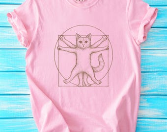 Puede incluir: Camiseta rosa con un gráfico de un gato al estilo del Hombre de Vitruvio, un famoso dibujo de Leonardo da Vinci.
