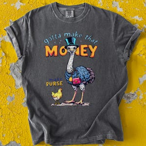 Puede incluir: Una camiseta gris con una avestruz de dibujos animados que lleva un sombrero de copa y un bolso. El texto "gotta make that MONEY" y "make PURSE" está impreso en la camiseta.
