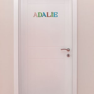 Pode incluir: Uma porta branca com uma ma&ccedil;aneta de porta prateada e o nome "ADALIE" escrito em letras coloridas na porta.