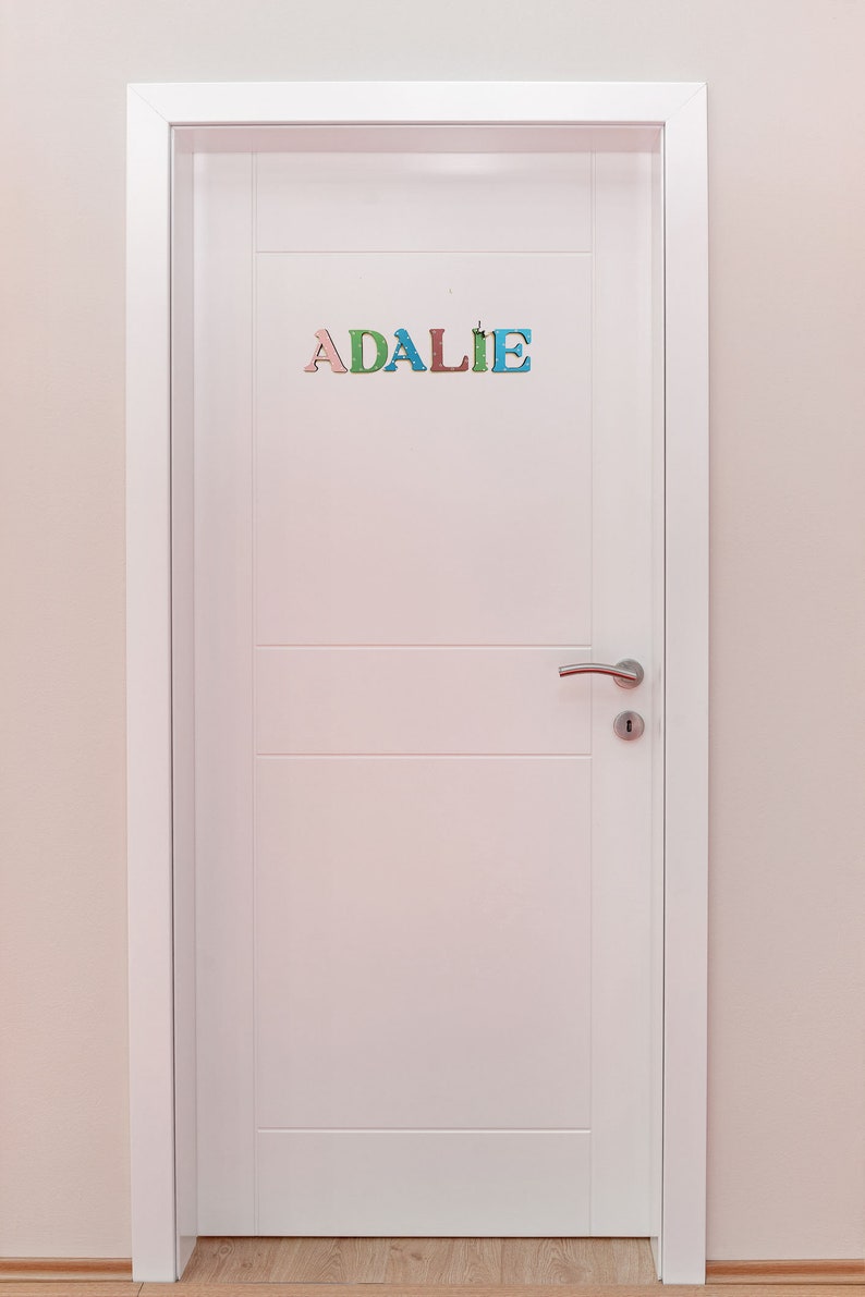 Pode incluir: Uma porta branca com uma ma&ccedil;aneta de porta prateada e o nome "ADALIE" escrito em letras coloridas na porta.