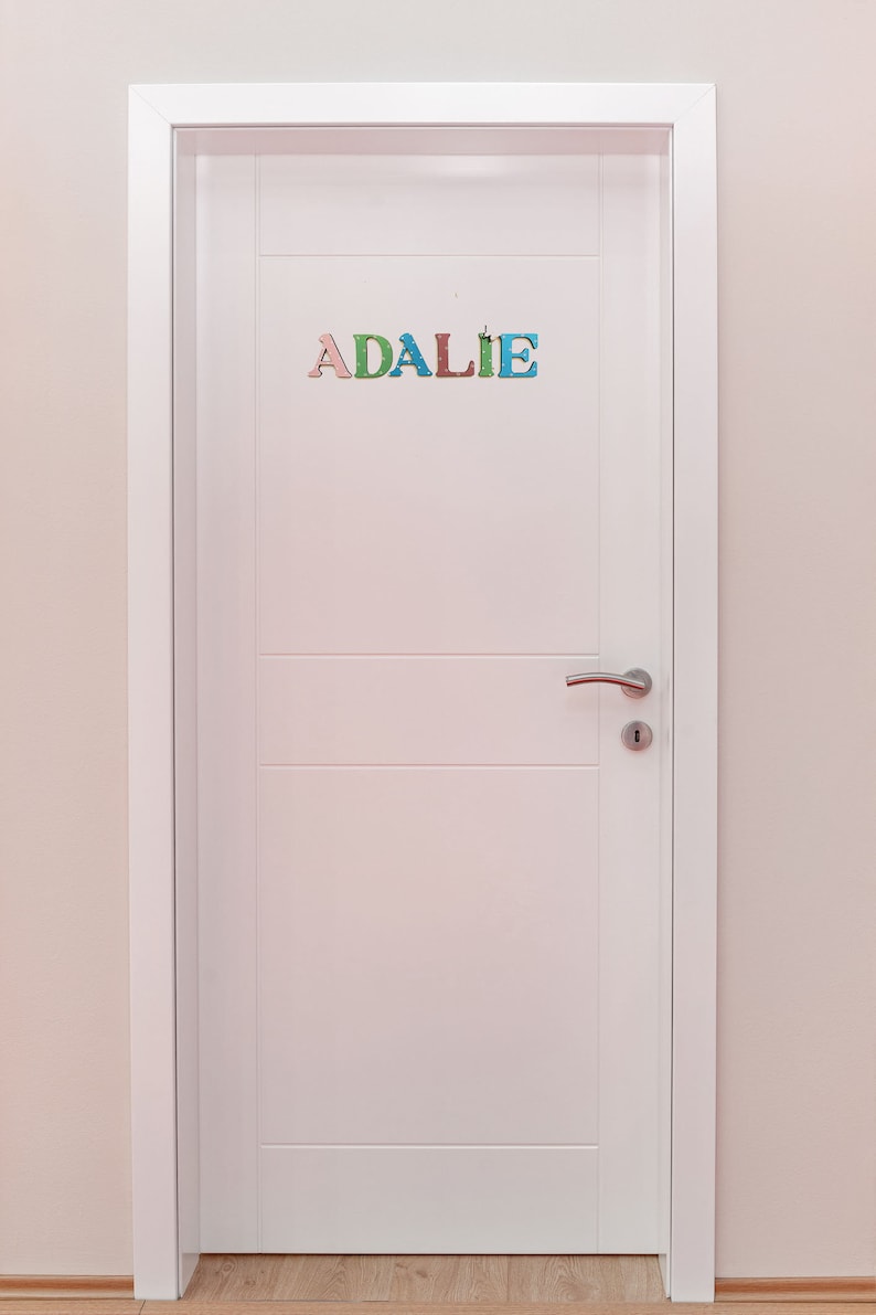 Pode incluir: Uma porta branca com uma ma&ccedil;aneta de porta prateada e o nome "ADALIE" escrito em letras coloridas na porta.