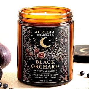 May include: A soy ritual candle in an amber glass jar with a black label featuring a gold crescent moon, botanical illustrations, and the text Aurelia Botanica Co. Black Orchard Dark Fig Juniper Berry Vetiver Patchouli 8 oz 227 g.