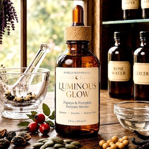 K&ouml;nnte beinhalten: Eine braune Glasflasche mit Aurelia Botanica Co. Luminous Glow Papaya & Pumpkin Enzym-Serum. Die Flasche hat einen Korken und eine Pipette. Das Etikett lautet "Hydratisiert, Gl&auml;ttet, Stellt Glanz wieder her" und "2 fl oz | 60 ml e".