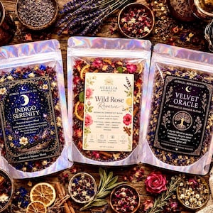 May include: Three holographic pouches containing botanical simmer blends labeled Indigo Serenity, Wild Rose Reverie, and Velvet Oracle. Each pouch features a unique decorative label with text, floral illustrations, and dried ingredients visible inside.