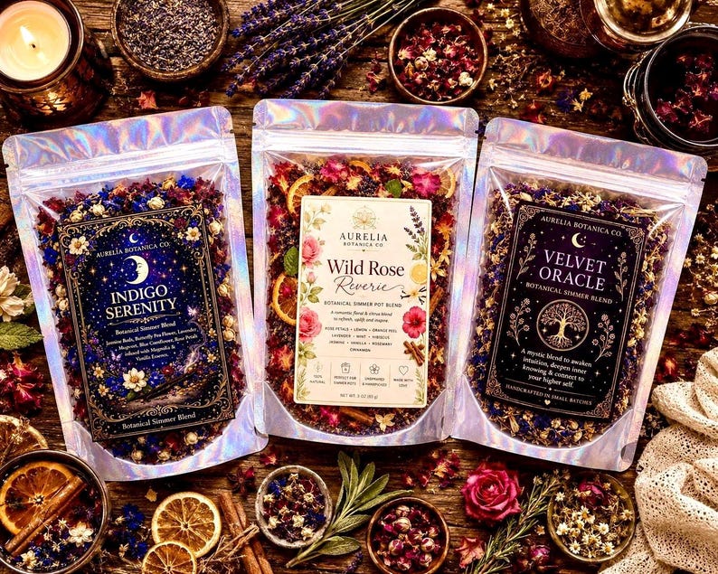 May include: Three holographic pouches containing botanical simmer blends labeled Indigo Serenity, Wild Rose Reverie, and Velvet Oracle. Each pouch features a unique decorative label with text, floral illustrations, and dried ingredients visible inside.