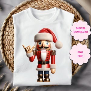 Pode incluir: T-shirt branca com um design festivo de quebra-nozes. O quebra-nozes veste um uniforme vermelho com detalhes dourados e um gorro de Pai Natal. A t-shirt também tem as palavras "DOWNLOAD DIGITAL" e "ARQUIVO PNG".