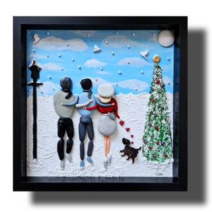 May include: A framed pebble art piece depicting a family of four walking in a snowy winter scene. The family are holding hands and walking towards a Christmas tree. A small dog is walking behind them. The artwork is set against a blue sky with white clouds and snowflakes.