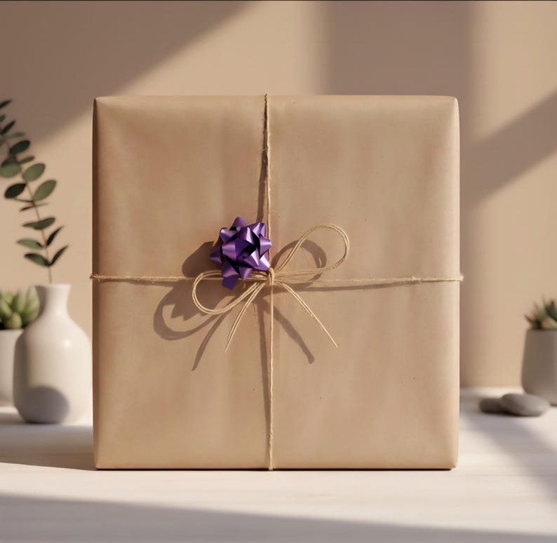 May include: A square gift box wrapped in plain light brown paper, tied with thin natural twine that forms a bow at the center. A small, shiny, metallic purple decorative bow is attached to the twine, positioned slightly above the center knot.