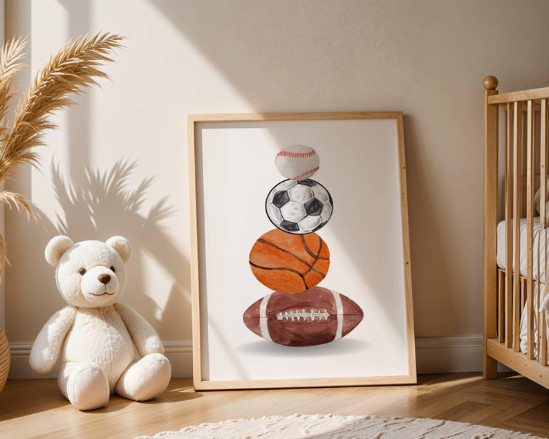 Pode incluir: Uma impress&atilde;o emoldurada com ilustra&ccedil;&otilde;es em aquarela de uma bola de beisebol, uma bola de futebol, uma bola de basquete e uma bola de futebol americano empilhadas. A obra de arte tem uma paleta de cores neutras e est&aacute; em uma moldura de madeira clara.