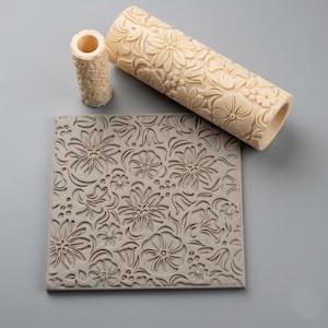 Peut inclure: Un rouleau à pâtisserie cylindrique beige avec un motif floral profond, un petit rouleau cylindrique assorti et un tapis carré plat présentant le même motif floral en relief. L'ensemble est composé d'un matériau solide de couleur claire.
