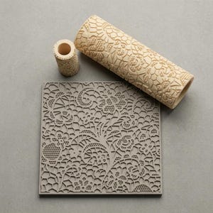 May include: A beige cylindrical rolling pin and a smaller matching cylindrical tool, both featuring a raised, intricate lace-like floral pattern. A square, flat, gray plate displays the same embossed, detailed floral lace design across its surface.
