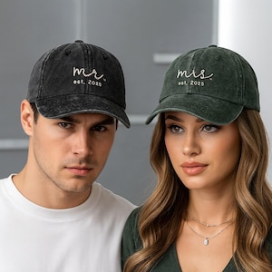 Puede incluir: Dos gorras de béisbol, una negra y otra verde, cada una con texto bordado. La gorra negra dice "mr. est. 2025" en cursiva. La gorra verde dice "mis. est. 2025". Ambas gorras tienen un aspecto desgastado y vintage.