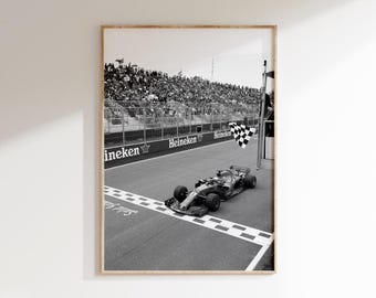May include: Black and white framed print of a Formula 1 race. A race car speeds across the finish line, with a checkered flag waving. The track has the word "Heineken" printed on it, and a crowd of spectators fills the background.