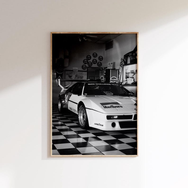 May include: Black and white framed print of a vintage race car. The car is white with black accents and the "Marlboro" logo. The background features a checkered floor and a "Pepsi" sign.