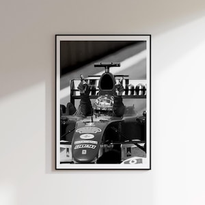 Könnte beinhalten: Schwarz-Weiß-Druck eines Formel-1-Rennwagens mit einem Fahrer, der den Sieg feiert. Der Fahrer, mit Helm, hebt beide Hände zum Victory-Zeichen. Das Auto zeigt Sponsorenlogos, darunter "Marlboro" und "Shell".