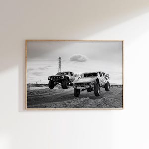 May include: Monochrome framed print depicting two off-road racing trucks in mid-air. The trucks display sponsor logos, including "Levi's" and "BFGoodrich". The background shows a cloudy sky and power lines.