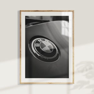 Puede incluir: Fotograf&iacute;a en blanco y negro enmarcada que presenta un primer plano del emblema de BMW. El emblema circular tiene un dise&ntilde;o negro y plateado, sobre un fondo gris oscuro. La fotograf&iacute;a est&aacute; en un marco de madera.