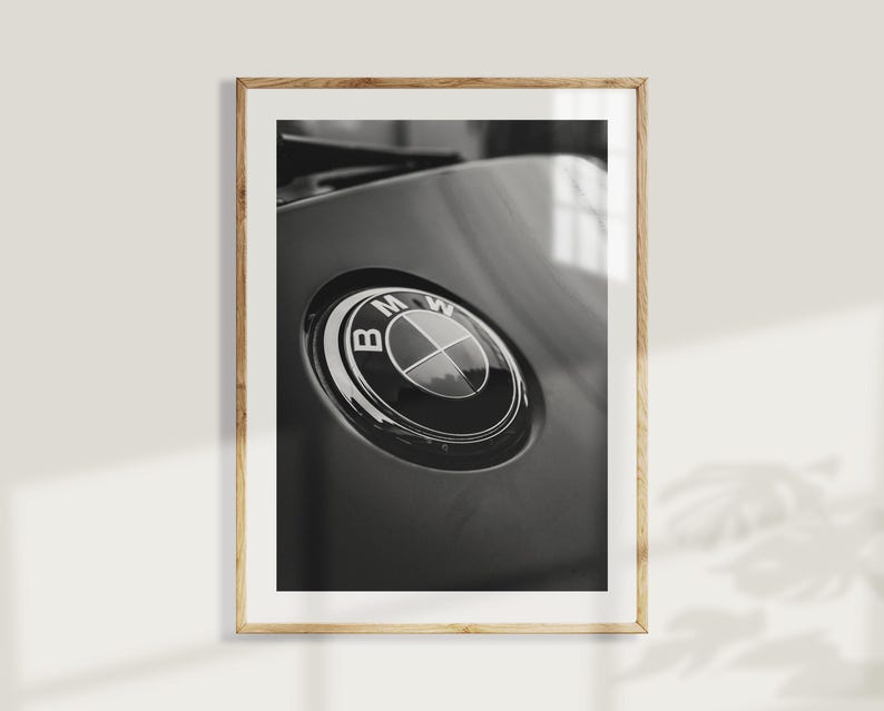 Puede incluir: Fotograf&iacute;a en blanco y negro enmarcada que presenta un primer plano del emblema de BMW. El emblema circular tiene un dise&ntilde;o negro y plateado, sobre un fondo gris oscuro. La fotograf&iacute;a est&aacute; en un marco de madera.