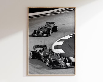 May include: Black and white framed print of two Formula 1 race cars speeding around a track corner. The cars are in motion, with visible details of the tires and aerodynamic design. The image is a high-angle shot.