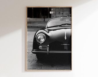 May include: Black and white framed print of a classic vintage car. The car's front features a round headlight, chrome bumper, and the hood ornament. The image is a close-up, highlighting the car's sleek design and glossy finish.