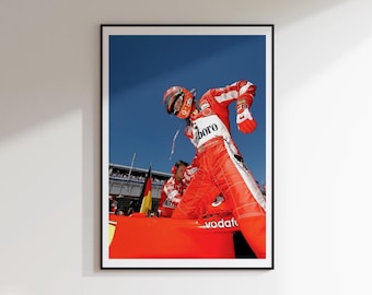 May include: A framed print featuring a Formula 1 driver in a red racing suit and helmet. The driver is leaning out of the car, with the Marlboro logo visible. The background is a clear blue sky.