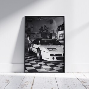 May include: Black and white framed print of a race car in a garage. The car is white with black accents and the Marlboro logo. The garage has a checkered floor and Pepsi signage.