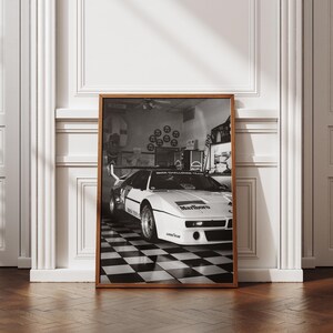 May include: Black and white framed print of a vintage race car. The car is white with black accents and the Marlboro logo on the front. The image is set in a garage with a checkered floor.