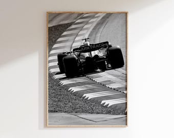 Puede incluir: Impresión enmarcada en blanco y negro de un coche de carreras tomando una curva. Se destacan la parte trasera y los neumáticos del coche. El texto "DARKTRACE" es visible en el alerón trasero. La pista tiene rayas blancas y grises.