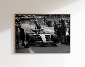 May include: Monochrome framed print depicting a Formula 1 car during a pit stop. The image shows the car surrounded by crew members in racing suits and helmets. The car is on a track marked with a white line.