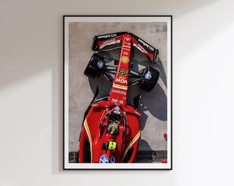 Könnte beinhalten: Eine Draufsicht auf einen roten Ferrari Formel-1-Rennwagen mit der Nummer 55, schwarzen Reifen und verschiedenen Sponsorenlogos wie HCLSoftware, Shell und VGW Play, präsentiert in einem schwarzen Rahmen an einer weißen Wand.