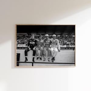 May include: Monochrome framed print showing four Formula 1 drivers in their racing overalls, seated on a wall. The image is a medium shot, with a crowd of spectators visible in the background.