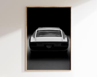 Op de afbeelding: Zwart-wit ingelijste print van een klassieke sportwagen, gezien vanaf de achterkant. De auto heeft een strak ontwerp met horizontale lamellen op de achterruit. De print wordt gepresenteerd tegen een witte muur.