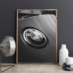 Puede incluir: Impresi&oacute;n enmarcada en blanco y negro que presenta un primer plano de un emblema de BMW. El emblema es circular con un anillo exterior negro y un anillo interior plateado, con el logotipo de BMW en el centro. La impresi&oacute;n se muestra sobre una superficie de madera.