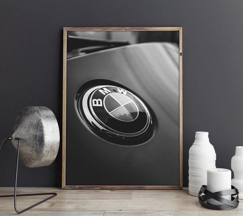 Puede incluir: Impresi&oacute;n enmarcada en blanco y negro que presenta un primer plano de un emblema de BMW. El emblema es circular con un anillo exterior negro y un anillo interior plateado, con el logotipo de BMW en el centro. La impresi&oacute;n se muestra sobre una superficie de madera.
